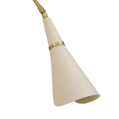 A close-up of a modern pendant light fixture showing a tapered off-white shade with a brushed brass band and matching brass rod against a solid light gray background.